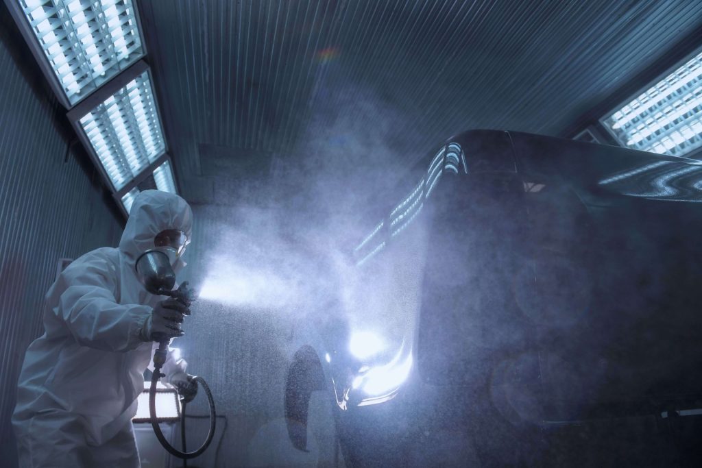 Technician spray painting a car in a paint booth
