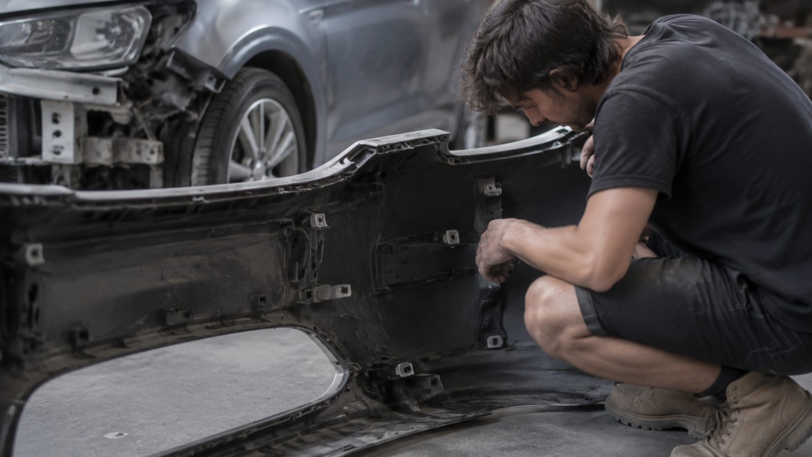 Technician inspecting brackets and mounts behind a removed bumper cover