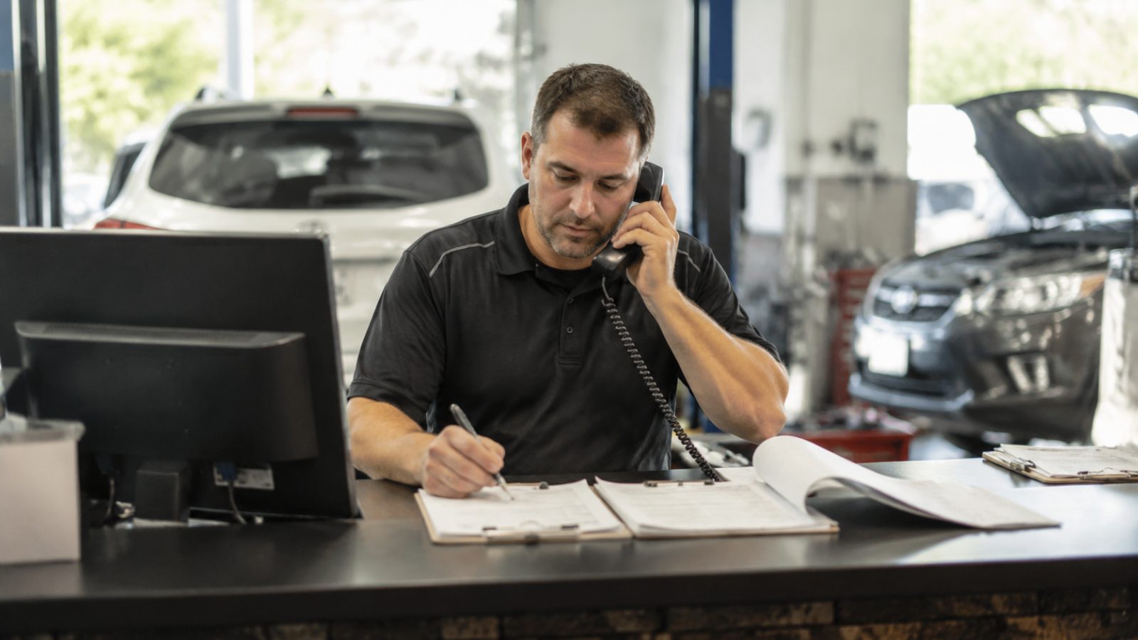 Service adviser at front counter on the phone with job card and parts order open