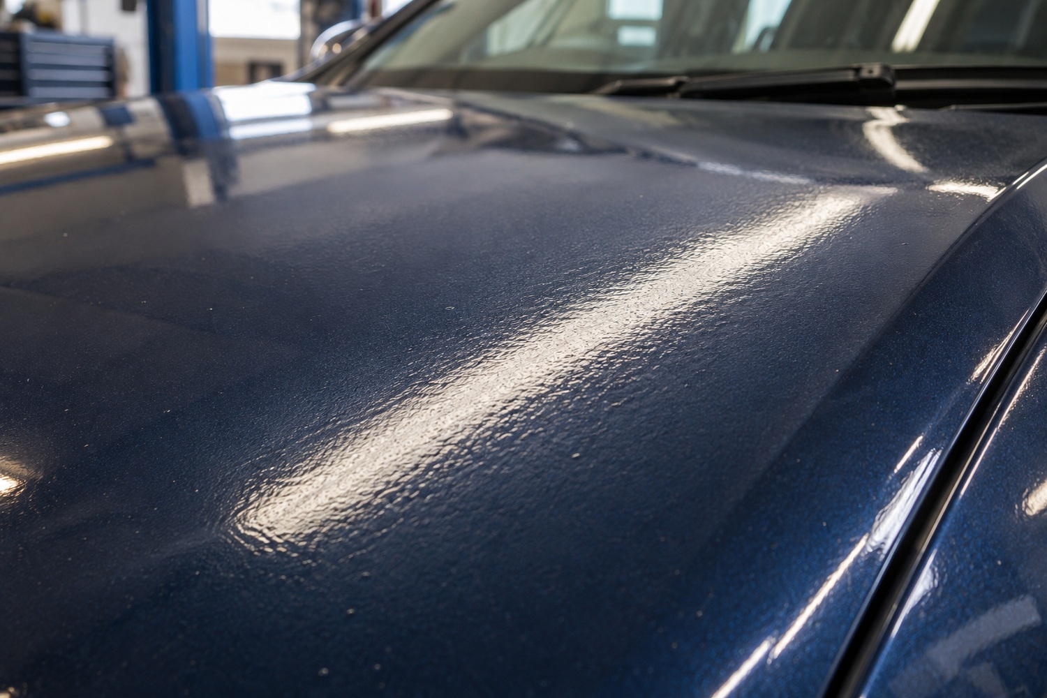 Raking light revealing orange-peel texture and small dust nibs in a blue bonnet's clearcoat.